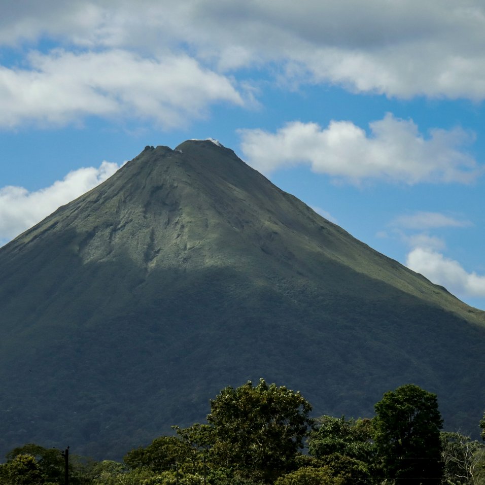 Volcán Arenal bajo un cielo azul con nubes